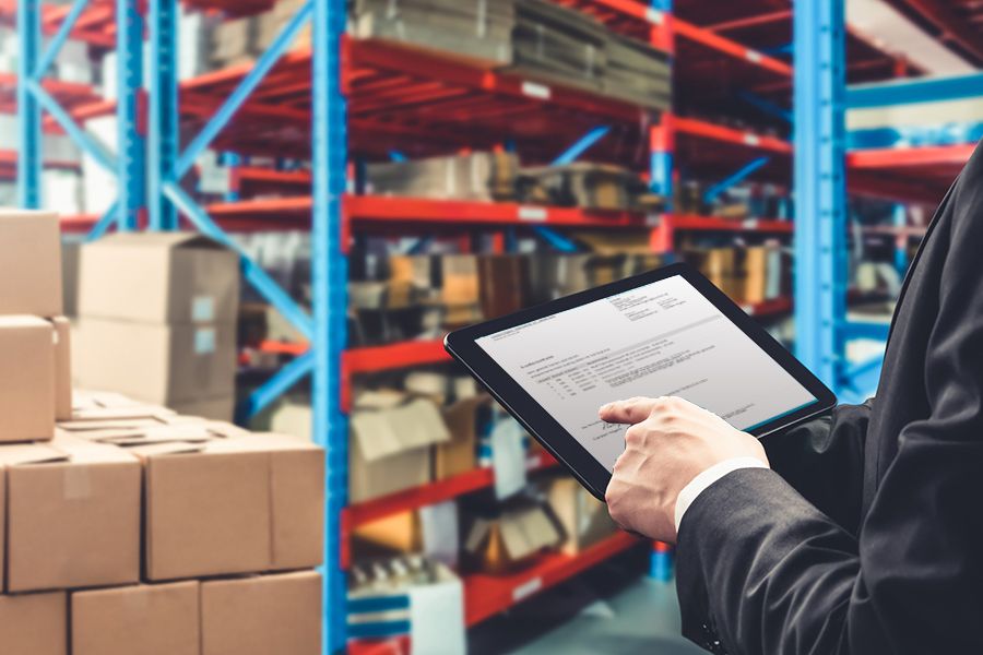 Mann im Anzug überprüft Lagerdokumente auf einem Tablet vor Regalen mit Kartons