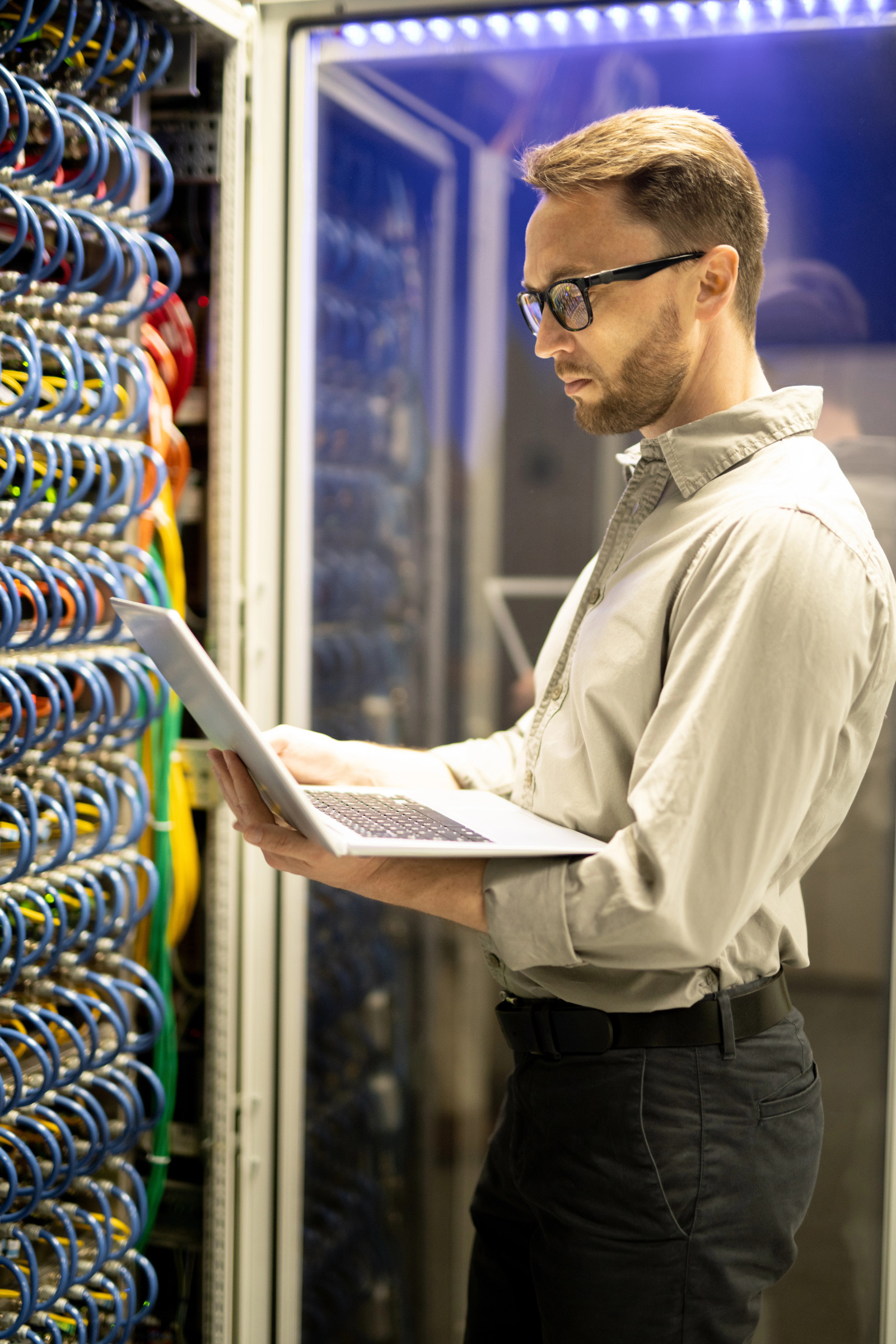 Mann mit Notebook vor Server Schrank